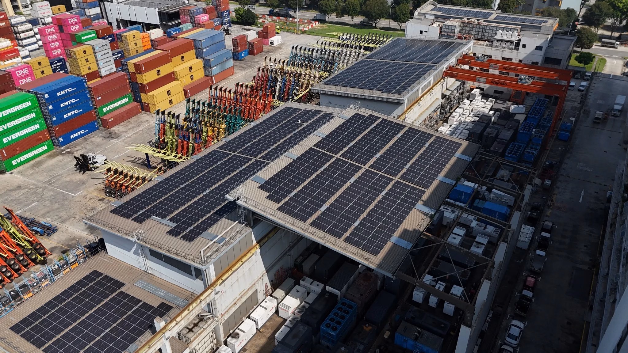 Aerial view of solar panels on commercial rooftops beside a shipping container yard in Singapore